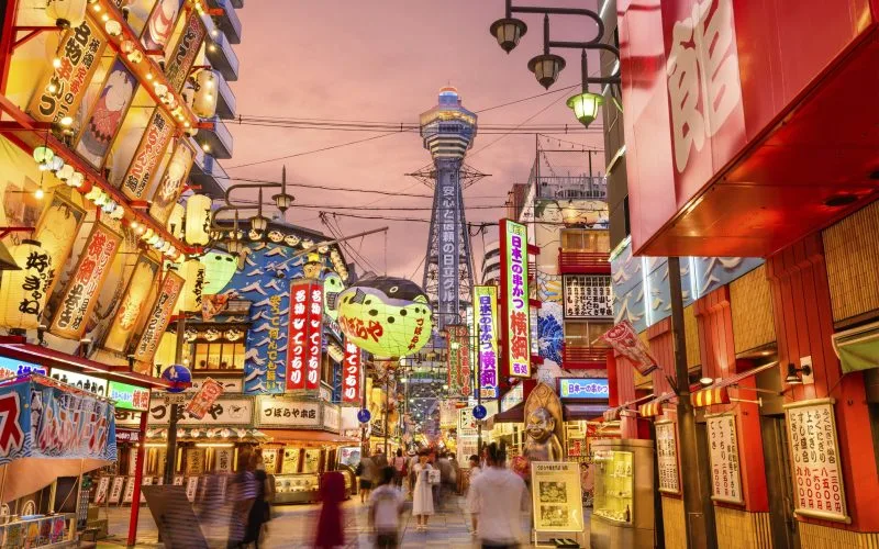 Tsūtenkaku tower glowing above the lantern-lit Shinsekai streets in Osaka — evening neighborhood walk with a local guide
